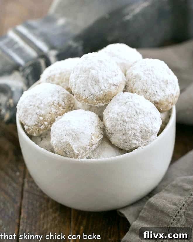 Irresistible Noel Nut Balls, adorned with powdered sugar and mixed with delightful toffee bits, presented in a pristine white dish.