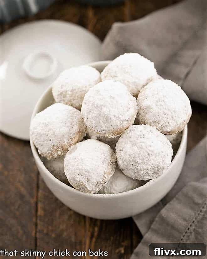 Overhead view of perfectly baked Noel Nut Balls, generously dusted with powdered sugar, arranged invitingly in a crisp white dish.