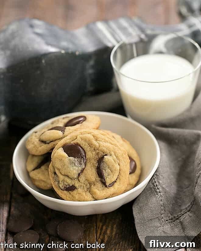 Southern Living's BEST Chocolate Chip Cookies in a white bowl next to a glass of milk, showcasing their thick, golden-brown edges and melted chocolate chunks.