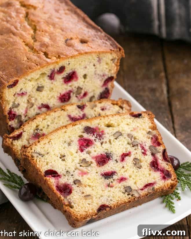 Slices of cranberry pecan quick bread on a white tray, showcasing vibrant cranberries and crunchy pecans.