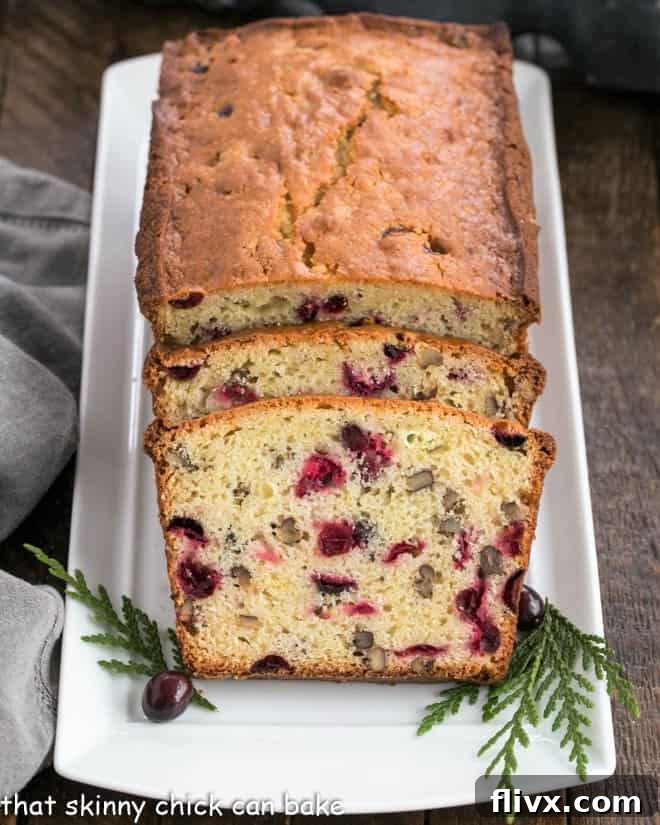 A baked loaf of cranberry pecan bread on a white tray with two perfect slices cut in front.