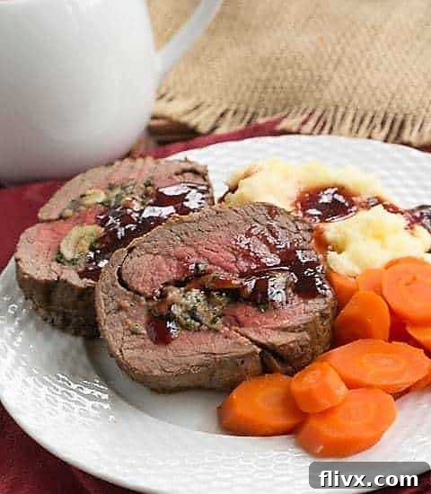 Elegantly plated slices of Gorgonzola and Mushroom Stuffed Beef Tenderloin with a rich red wine sauce, ready to be served at a holiday dinner.