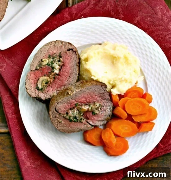 Close-up of freshly sliced Gorgonzola and Mushroom Stuffed Beef Tenderloin, showcasing the spiral filling and juicy texture, on a white dinner plate.