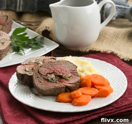 A generous serving of Gorgonzola and Mushroom Stuffed Beef Tenderloin, perfectly sliced, accompanied by roasted carrots and creamy mashed potatoes on a elegant dinner plate.