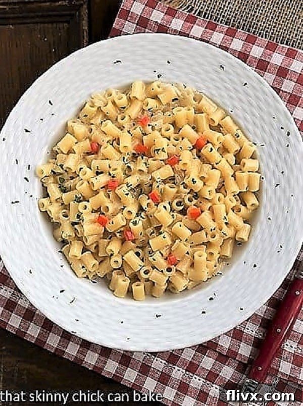 Overhead view of pasta risotto in a white bowl on a red and white checkered napkin, garnished with fresh herbs