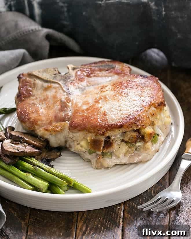 A beautifully Stuffed Pork Chop on a white dinner plate, garnished with fresh asparagus and mushrooms.