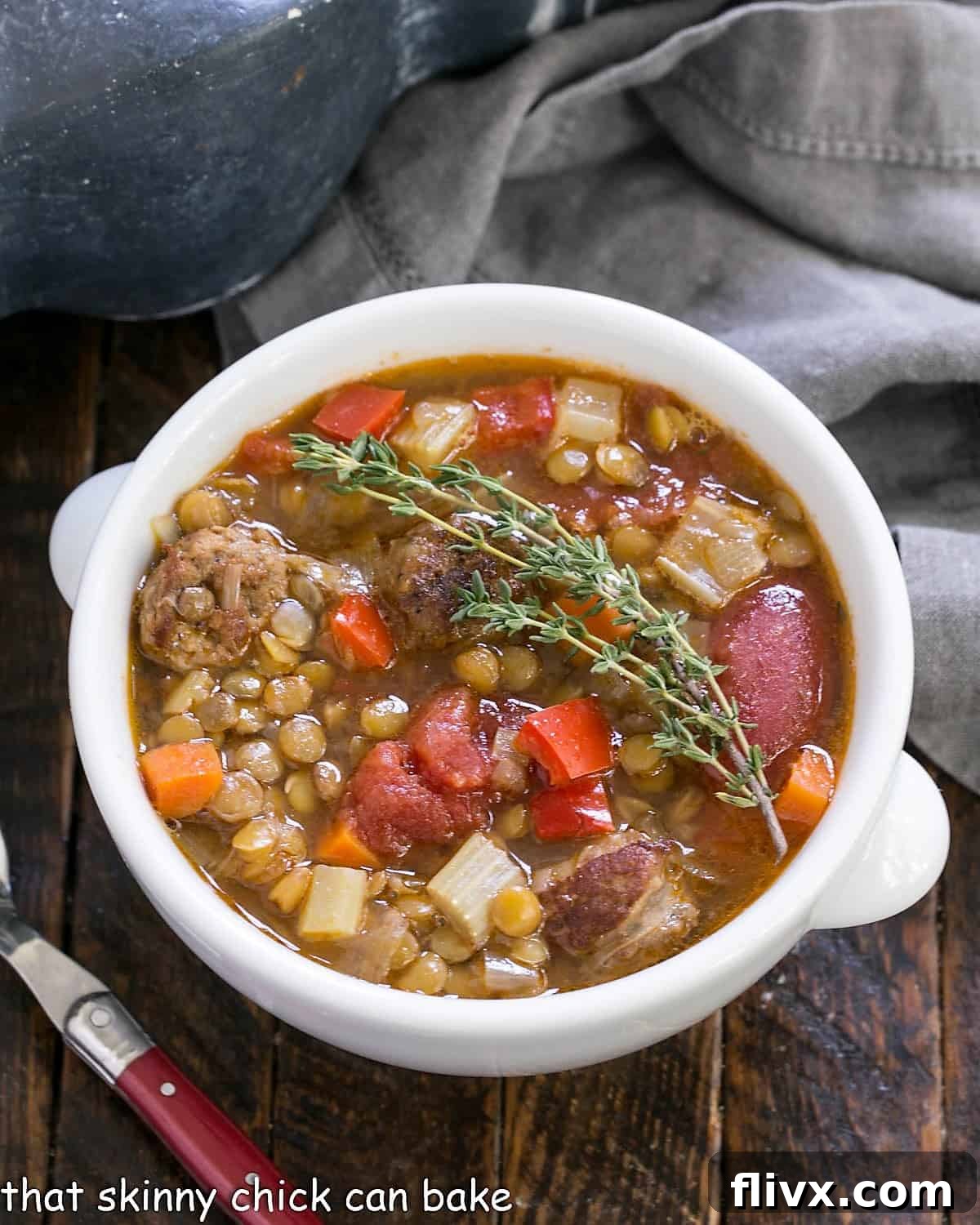 Overhead view of a white bowl of Sausage Lentil Soup, garnished with fresh thyme leaves, ready to be enjoyed.