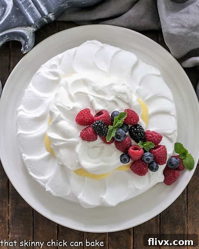 Overhead view of a pavlova dessert topped with lemon cream, whipped cream and berries