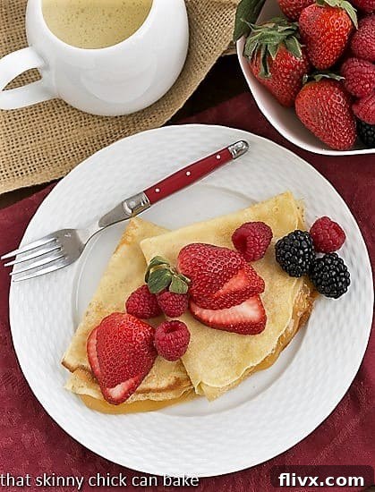 Overhead view of several golden Butter and Rum Crêpes arranged beautifully on a white plate with a striking red-handled fork.