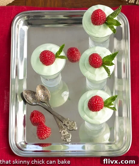 Close-up aerial view of rich Grasshopper Mousse presented on a sleek silver platter, beautifully adorned with fresh raspberries and elegant spoons, highlighting its creamy texture and vibrant color.