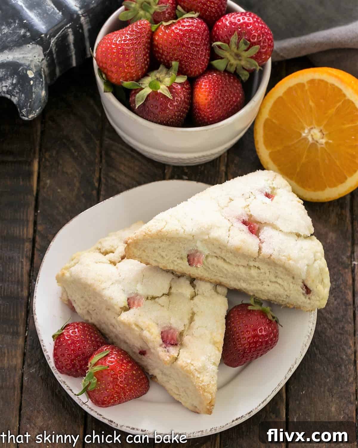 Overhead view of two golden-brown Strawberry Buttermilk Scones on a small white plate, adorned with fresh, ripe strawberries.