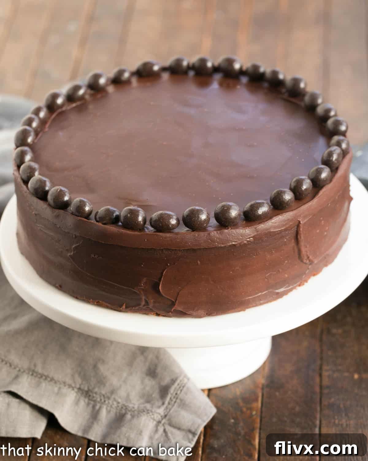 A stunning Mocha Brownie Cake proudly displayed on a white ceramic cake stand, ready to be admired and enjoyed. Its dark, glossy ganache hints at the rich flavors within.