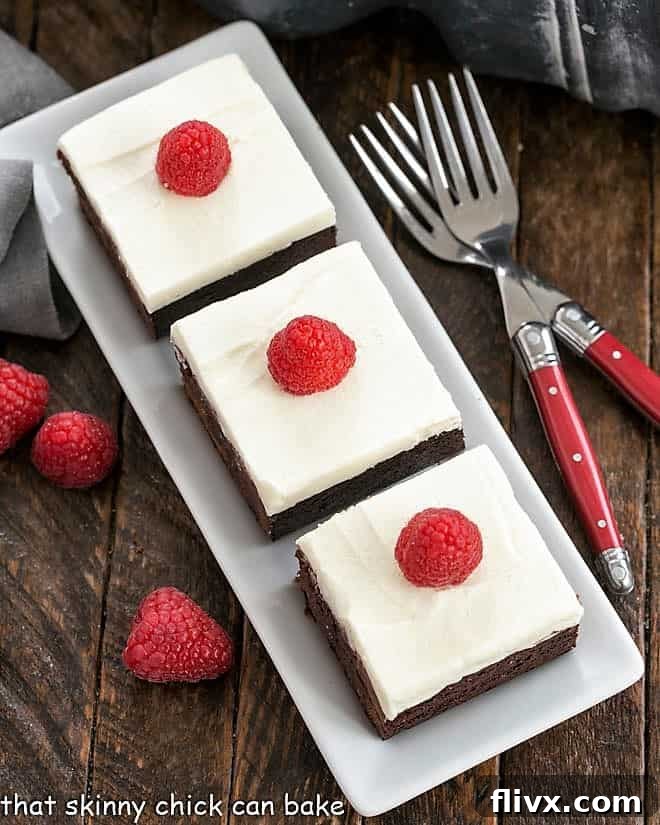 Overhead view of fudgy Raspberry Chambord Brownies topped with creamy white chocolate frosting on an elegant white serving tray, ready to impress.