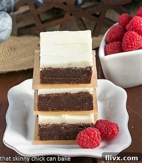 Close-up of a perfectly frosted Raspberry Brownie on a small white plate, with a bottle of Chambord liqueur in the background, highlighting the key flavor.