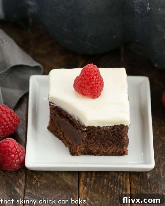 A perfectly portioned, frosted Raspberry Chambord Brownie on a square white plate, with a bite taken to reveal its fudgy interior and raspberry swirls.