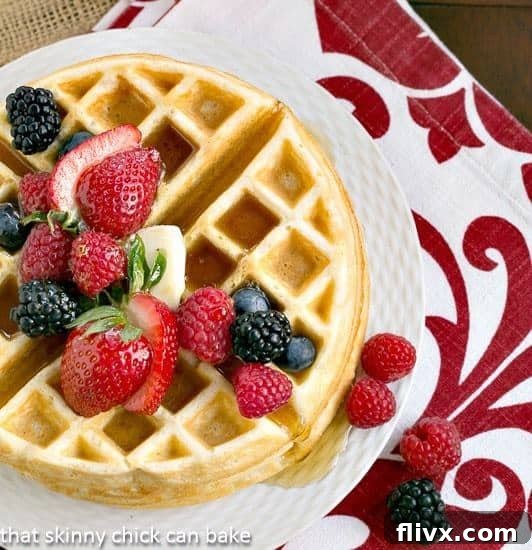 A stack of golden brown Homemade Buttermilk Waffles on a white plate, garnished with fresh mixed berries.