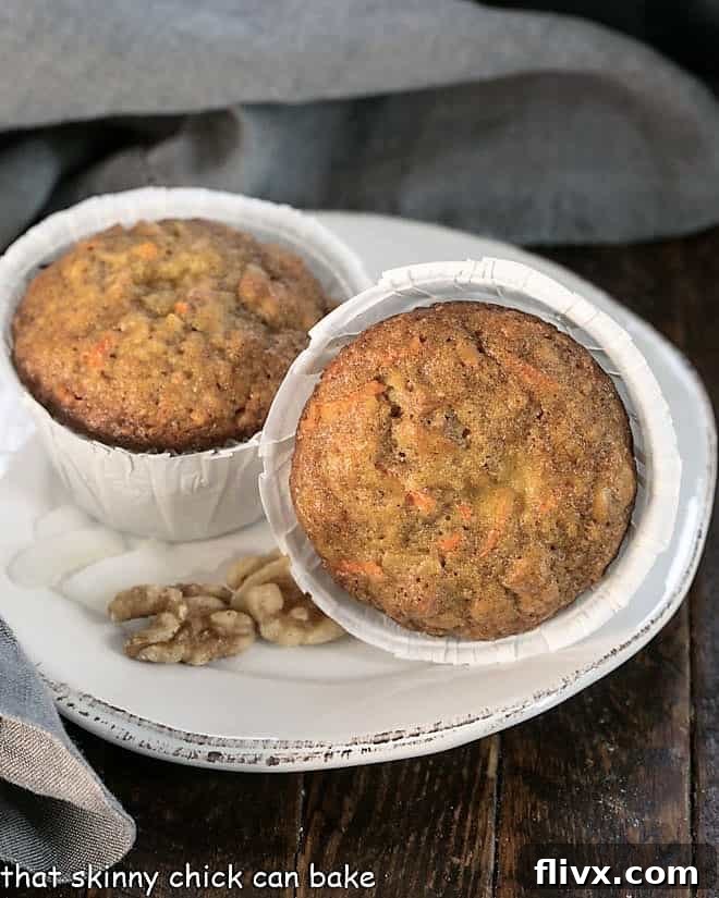 Two perfectly golden and inviting Cream Cheese Filled Carrot Cake Muffins, presented on a minimalist round white plate, ready to be enjoyed.