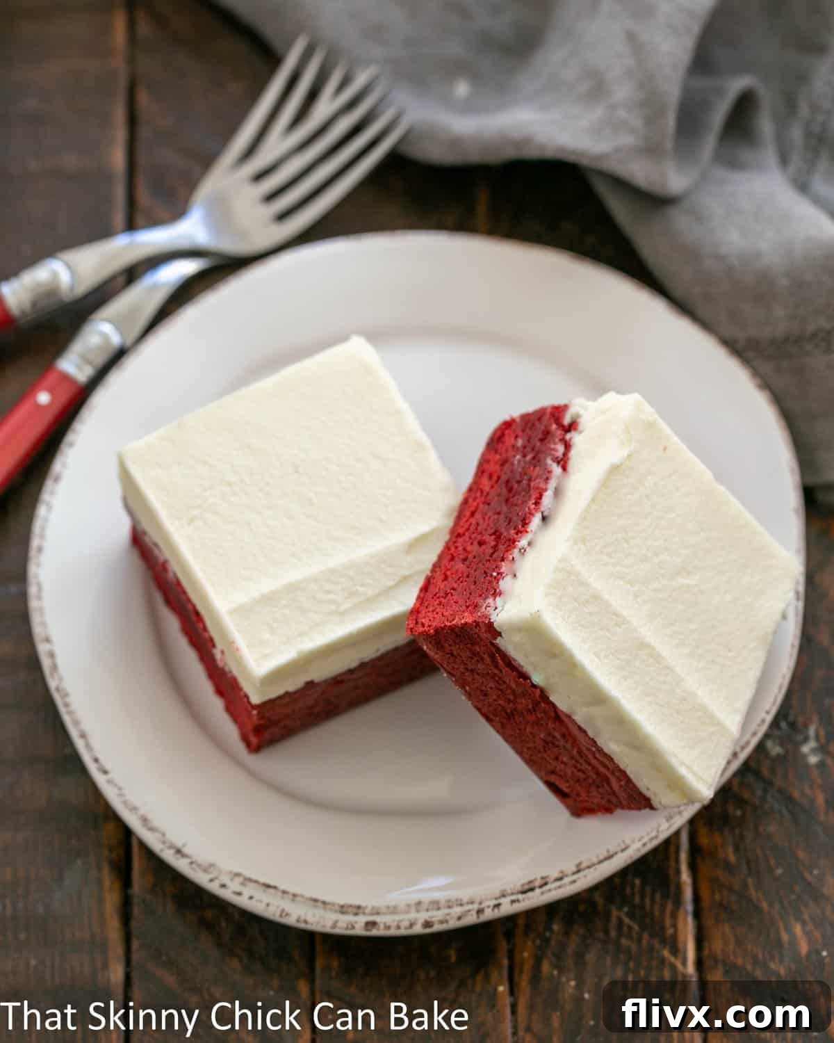 An overhead view of two vibrant red velvet brownies, beautifully presented on a white dessert plate, with a luxurious white chocolate icing perfectly contrasting the rich red hue. Ideal for special occasions or a decadent everyday treat.