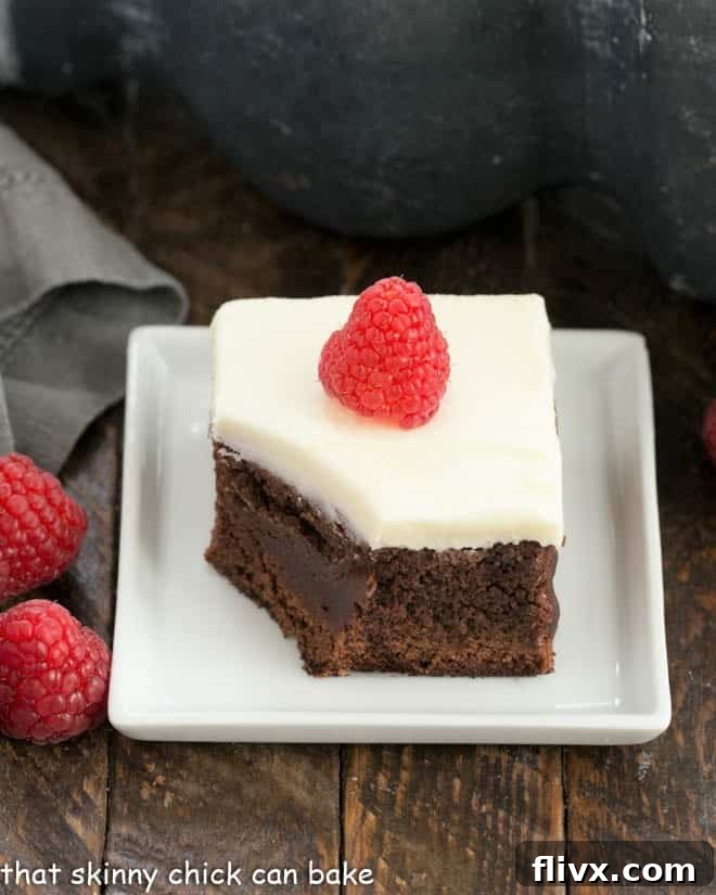 A tempting Raspberry Chambord Brownie, served on a pristine white plate, with a small bite removed to reveal its luscious interior. The rich chocolate and vibrant raspberry hues promise a sophisticated and flavorful dessert.
