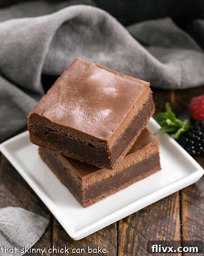 Two perfectly stacked Chocolate Cheesecake Brownies resting on a modern square white dish, showcasing the delightful layers of rich chocolate and creamy cheesecake, inviting you to indulge.