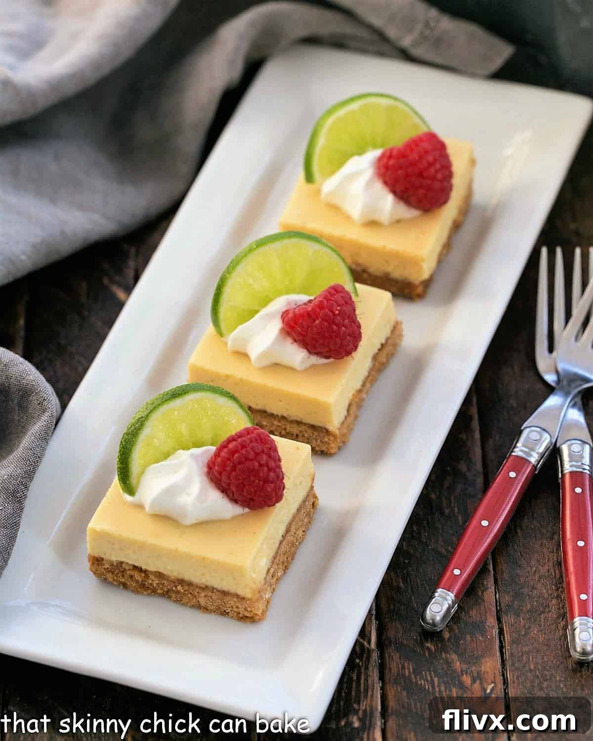 3 key lime pie bars garnished with whipped cream, lime slices and fresh raspberries on a white tray.
