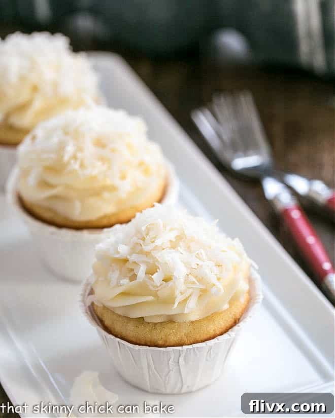 Deliciously moist coconut cupcakes with a generous swirl of cream cheese frosting on a pristine white serving tray, garnished with shredded coconut.