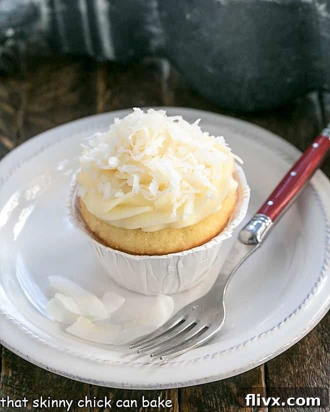 Close-up of a single coconut cupcake with fluffy cream cheese frosting, elegantly placed on a small white plate, ready to be enjoyed.