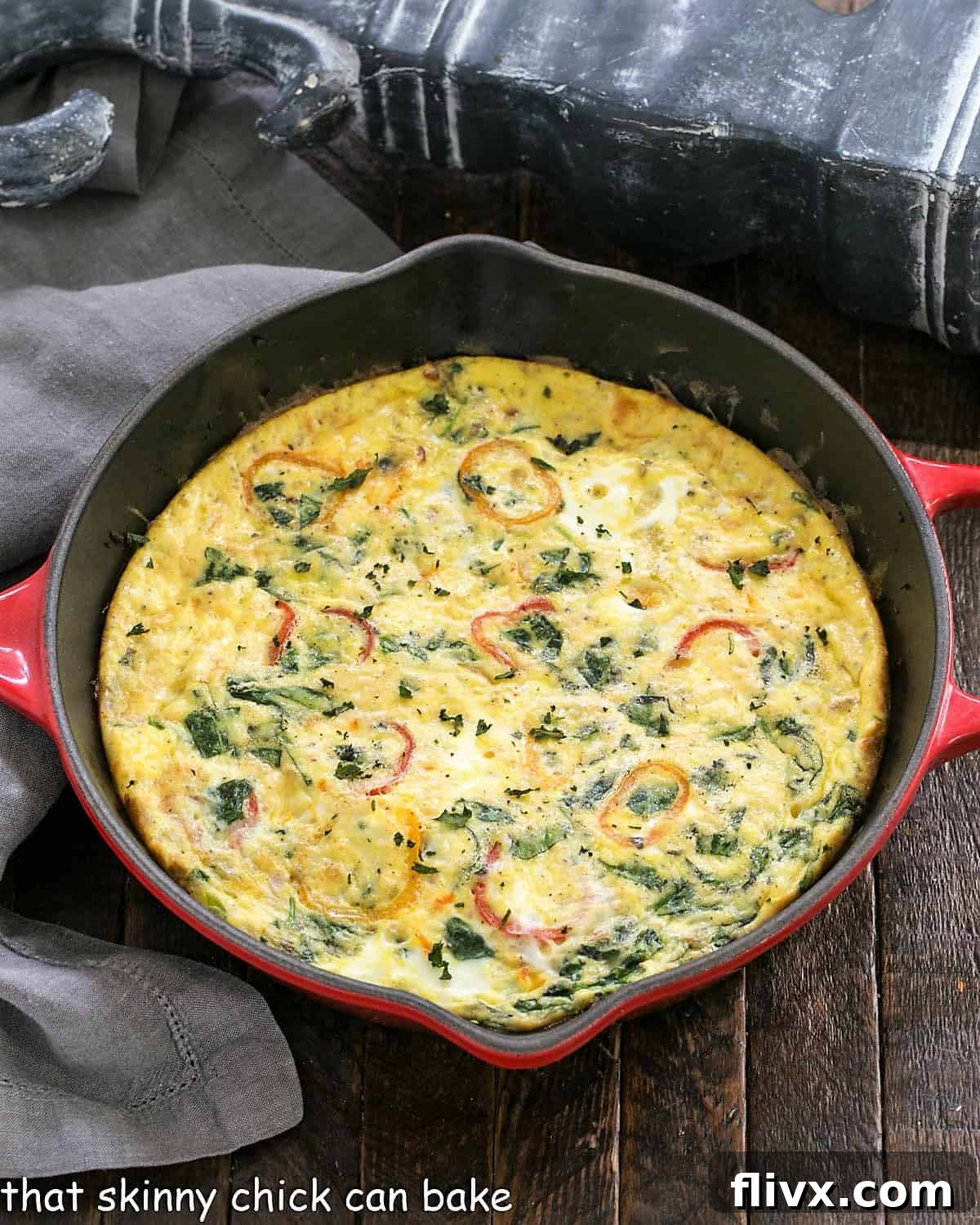 Overhead close-up view of a perfectly cooked, golden-brown Spinach Frittata nestled in a vibrant red cast iron skillet, ready to be served.