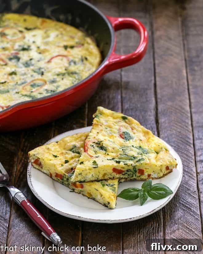 Two generous slices of a fluffy breakfast frittata are presented on a clean white plate, with the rustic red cast iron skillet, where it was cooked, visible in the background.