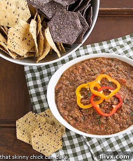 A close-up shot of Smoky Black Bean Dip in a rustic white bowl, accompanied by a bowl of golden, crunchy tortilla chips.