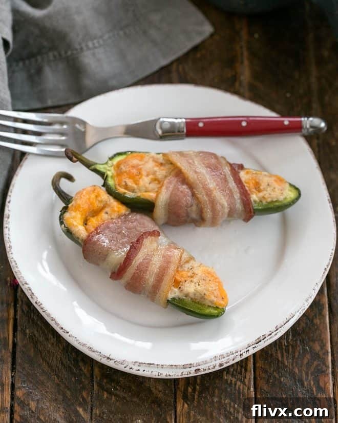 Two perfectly cooked bacon-wrapped jalapeno poppers on a round white plate, ready to be enjoyed with a red-handled fork.