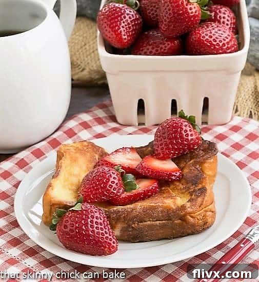 Strawberry Mascarpone Stuffed French Toast on a white plate topped with fresh strawberries and a dusting of powdered sugar.