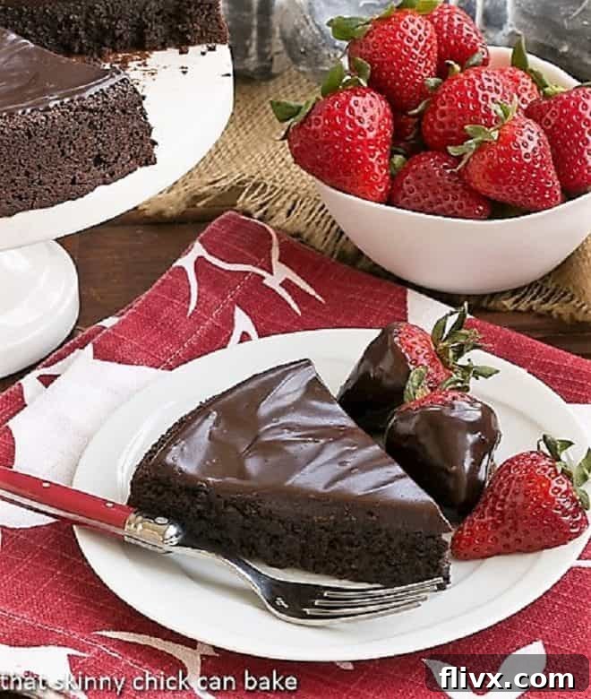 Flourless Double Chocolate Cake slice on a white plate with chocolate covered strawberries, highlighting its dense, fudgy texture.