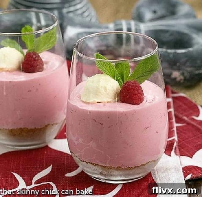 Raspberry Mousse in elegant parfait glasses, beautifully garnished with fresh whipped cream, whole raspberries, and a delicate sprig of mint, showcasing its delightful layers and vibrant color.