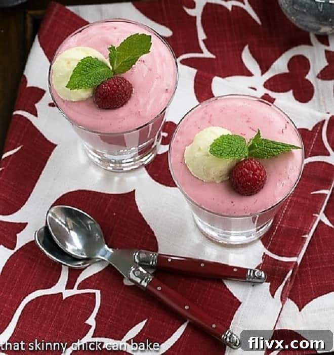 Two servings of Raspberry Mousse presented in highball glasses, photographed from a top-down perspective, with elegant red-handled spoons resting on a festive red and white striped napkin, highlighting the dessert's appealing texture and presentation.