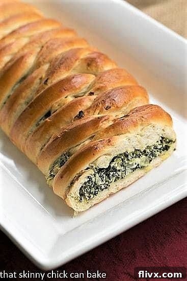 A beautifully golden-brown Spinach and Onion Braid on a long white platter, with a cross-section revealing the rich, green, cheesy filling.