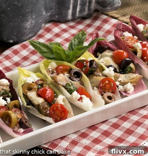 A white ceramic tray filled with crisp endive leaves brimming with a colorful Mediterranean salad, ready to be served.