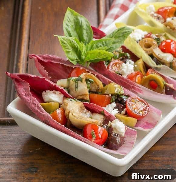 Close view of Mediterranean Endive Boats in a white, rimmed serving tray, with vibrant colors of olives, tomatoes, and feta.