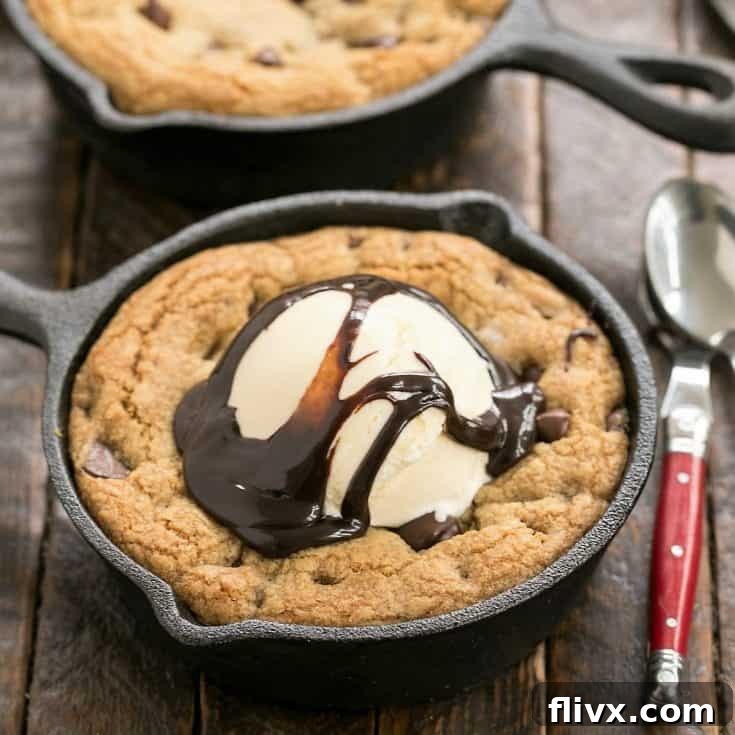 An irresistible homemade pizookie served in a skillet, generously topped with vanilla ice cream and chocolate fudge sauce, with a red spoon taking a bite.
