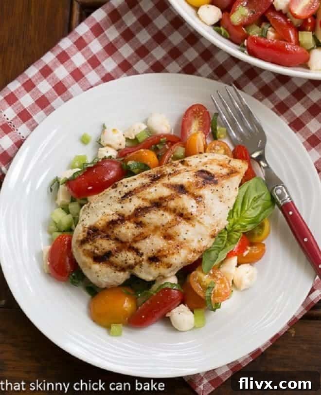 Overhead view of grilled chicken breast elegantly arranged over a fresh Caprese salad, showcasing vibrant colors.