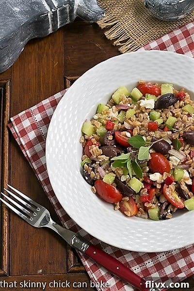 An overhead shot of Greek Farro Salad beautifully arranged in a white bowl, resting on a charming red and white checked napkin.