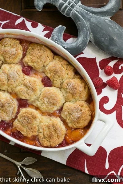 A vibrant Peach Raspberry Cobbler, still warm from the oven, showcasing its golden biscuit topping and bubbling fruit filling.