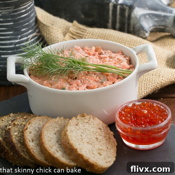 A large serving of Salmon Rillettes on a white plate, garnished with fresh herbs and a slice of lemon.