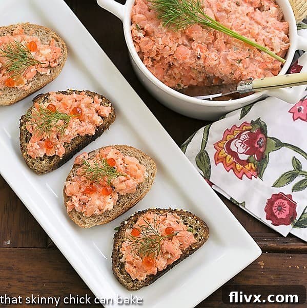 A white platter holding toasts topped with Salmon Rillettes, alongside a terrine of the salmon spread.