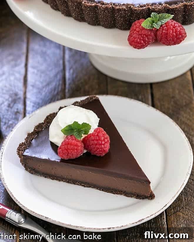 A perfectly sliced Ganache Topped Chocolate Tart, garnished with fresh whipped cream, vibrant berries, and a sprig of mint, showcasing its luscious layers.