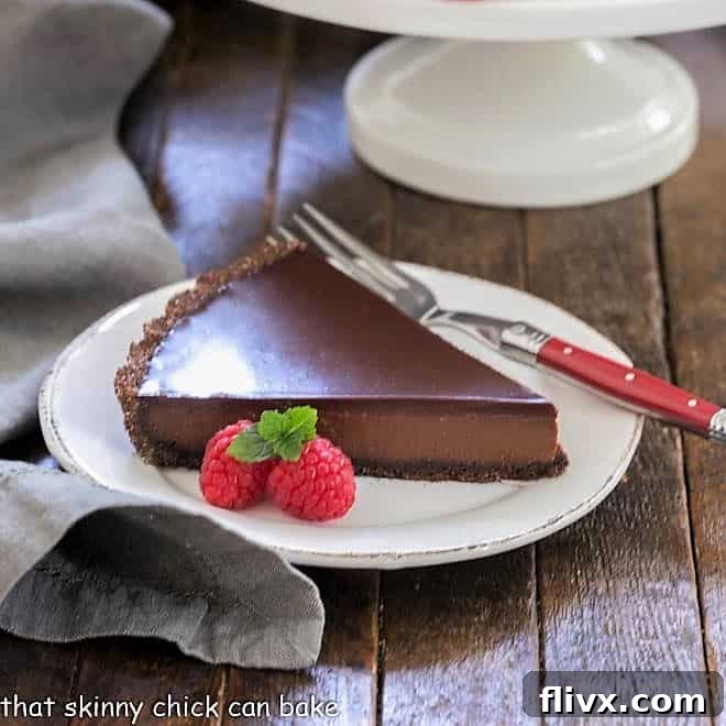A beautiful slice of chocolate tart on a round white plate with a red fork, ready to be enjoyed.