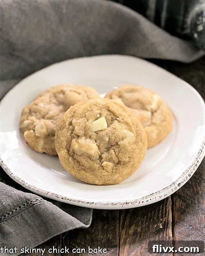 Three perfectly golden White Chocolate Macadamia Nut Cookies stacked on a white plate, showcasing their inviting texture.