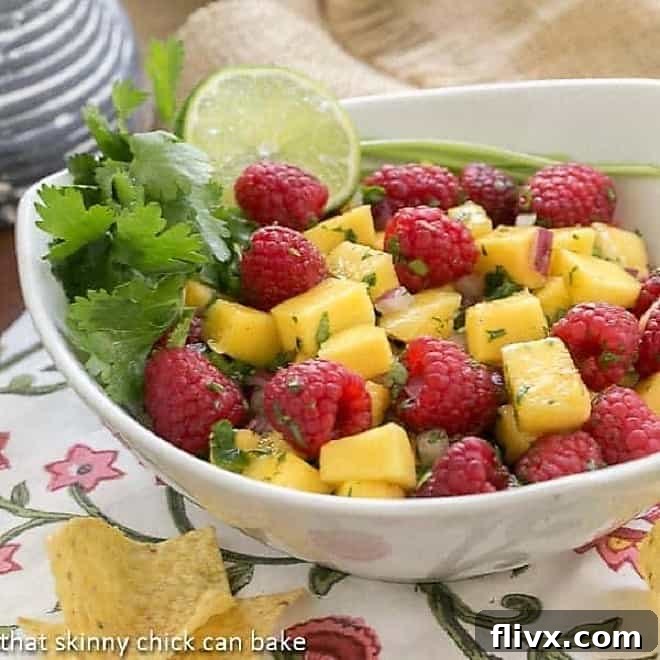 Vibrant Raspberry Mango Salsa in a pristine white bowl, garnished with fresh cilantro and a wedge of lime.
