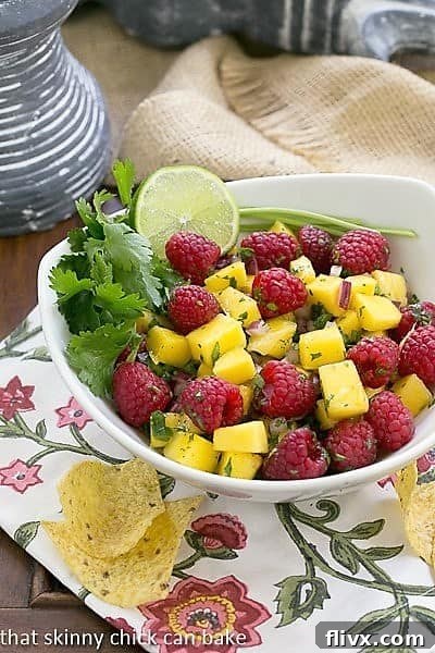 Close-up of vibrant Raspberry Mango Salsa in a white bowl, garnished with fresh cilantro and a lime wedge, ready to be served.