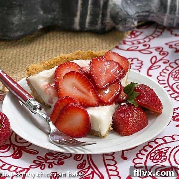 A perfectly sliced piece of Strawberry Cheesecake Ice Cream Pie, revealing creamy layers and a crumbly crust, served on a white dessert plate with a few fresh strawberry garnishes